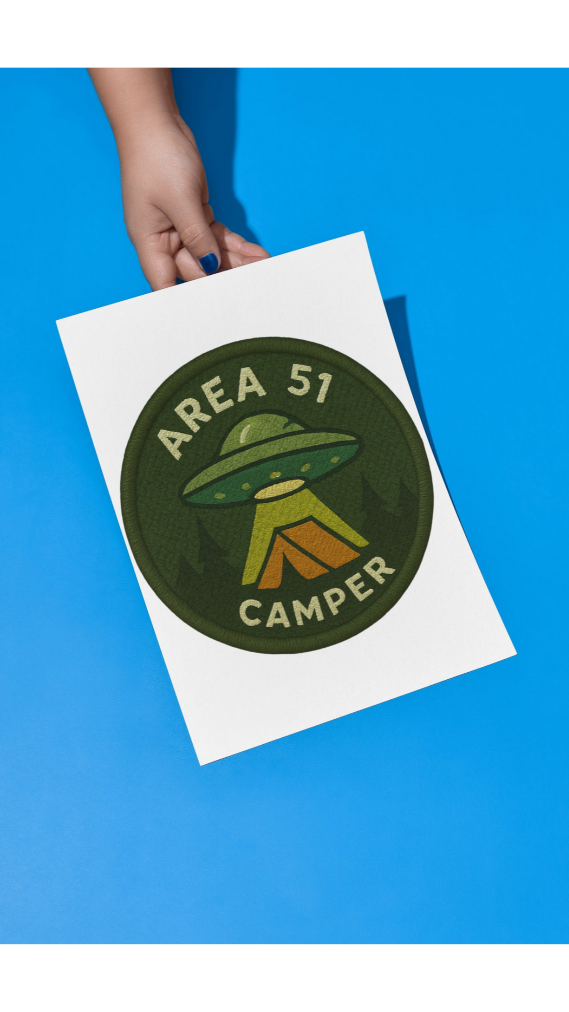 Sticker with 'Area 51 Camper' design held by a hand on a blue background