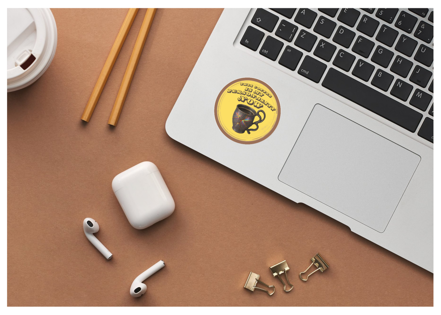 Laptop with a coffee-themed sticker, airpods, and office supplies on a brown surface