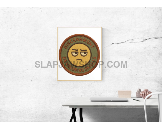 Framed artwork of a sad emoji on a white wall above a desk.