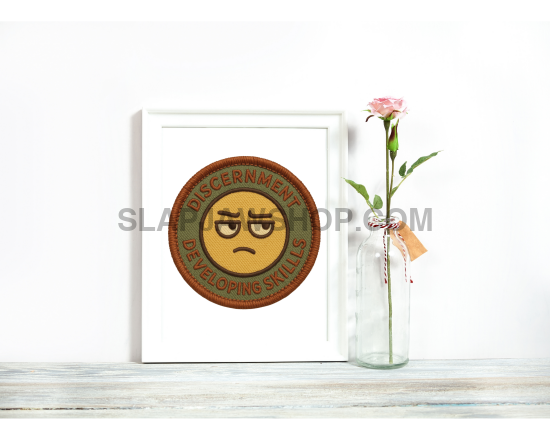 Framed artwork with a sad face emoji next to a vase with flowers on a white background