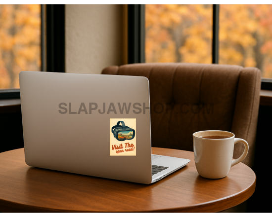 Laptop with a sticker on a wooden table in front of a window with autumn foliage.